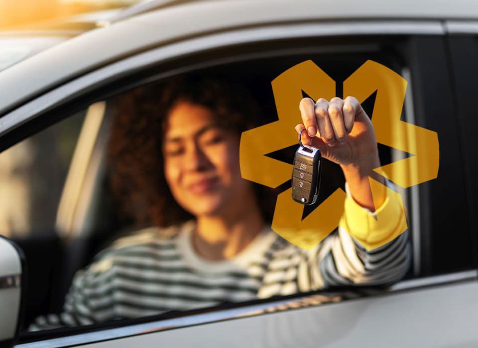 Woman sitting in a car holding up a key fob with a proud smile.