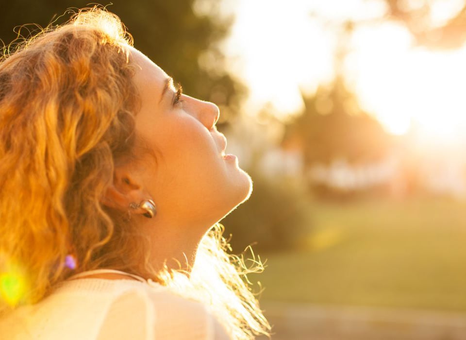 Woman peacefully gazing toward the sun during golden hour, surrounded by soft, warm light.