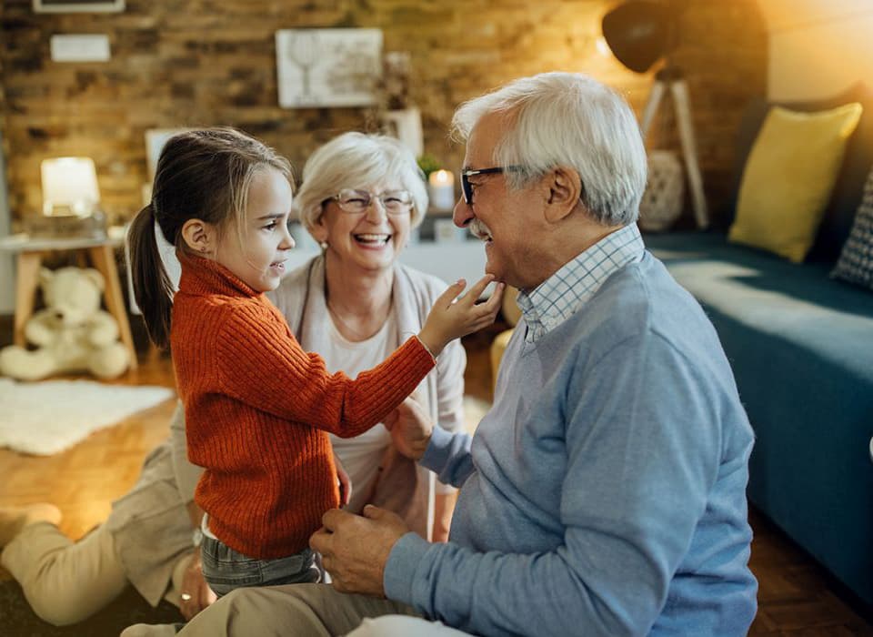 Smiling grandparents sharing a joyful moment with their granddaughter at home.
