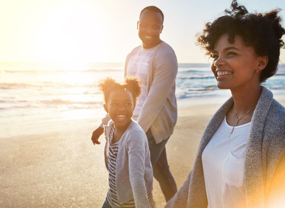 Smiling family walking along the beach at sunset, enjoying time together in the warm light.